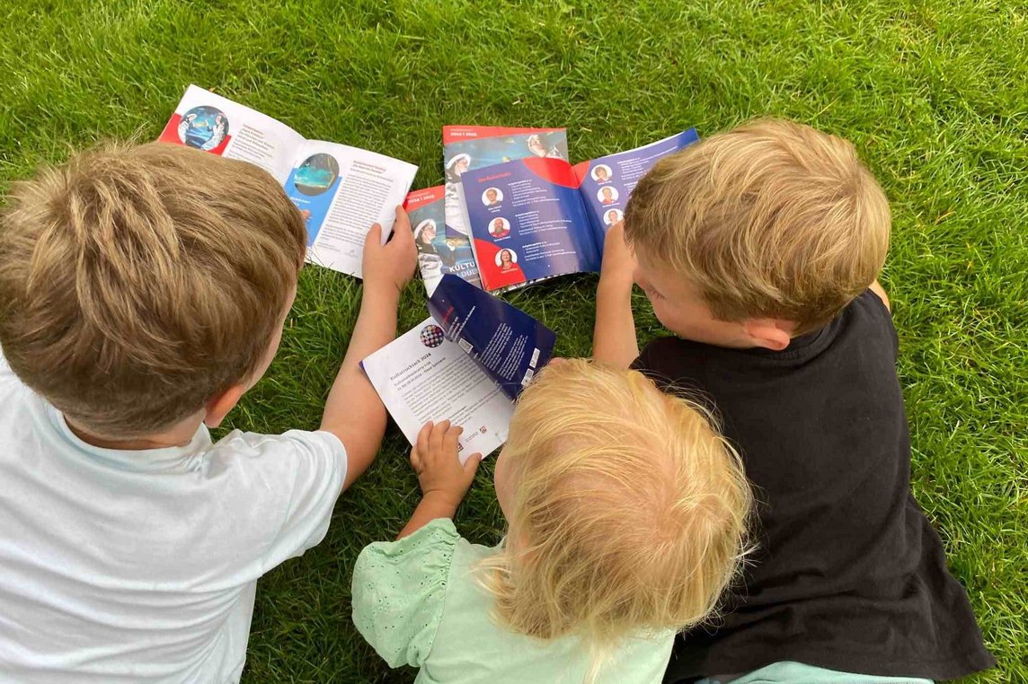 Dieses Foto zeigt Kinder, die das neue Programmheft "Kultur für Kids" studieren